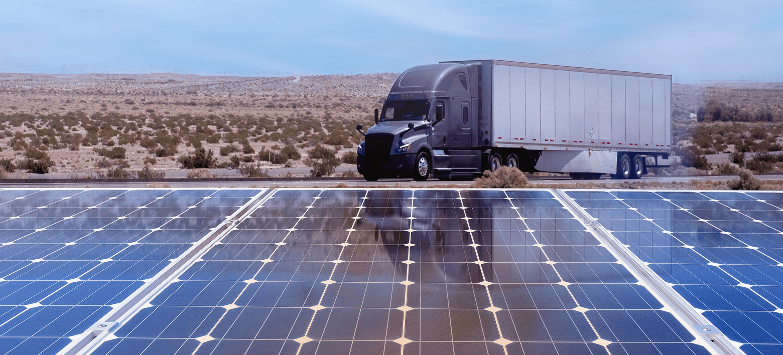 A semi-truck in a desert landscape, with a large array of solar panels in the foreground.